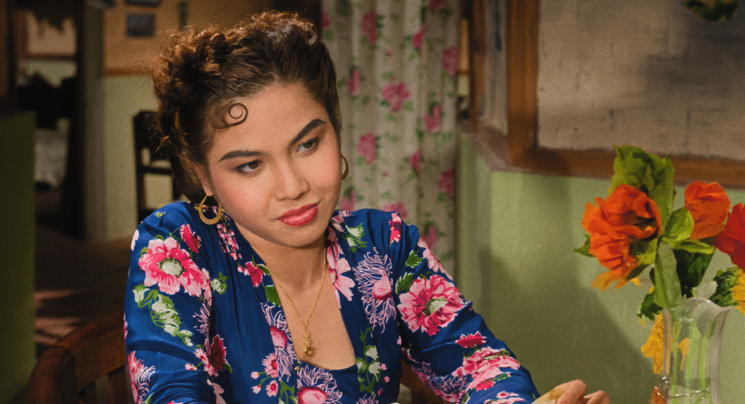Colourised close-up of a woman in a blue floral robe beside flowers and patterned curtains