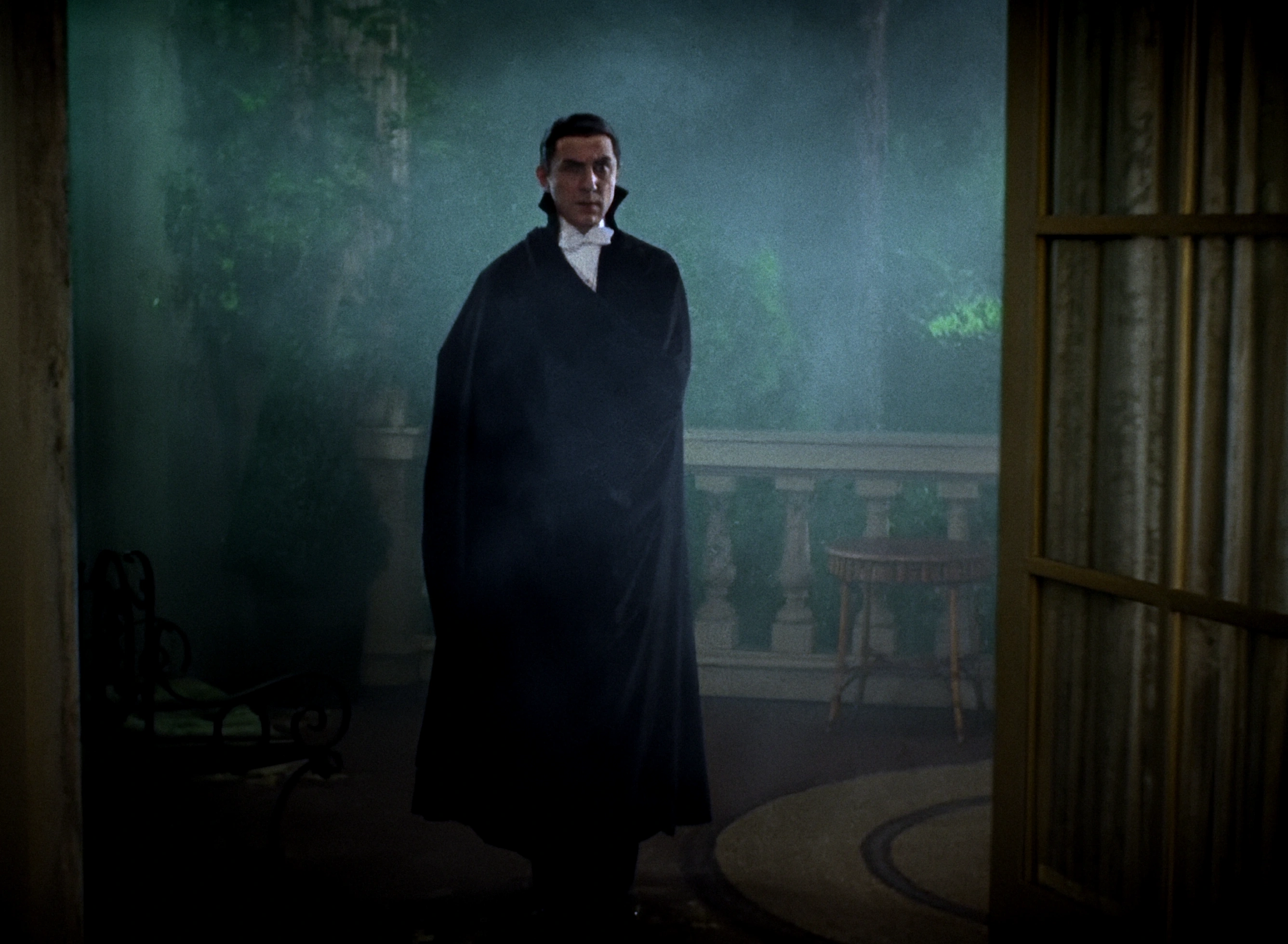 Colourised film still of a cloaked figure in a misty, blue-green interior