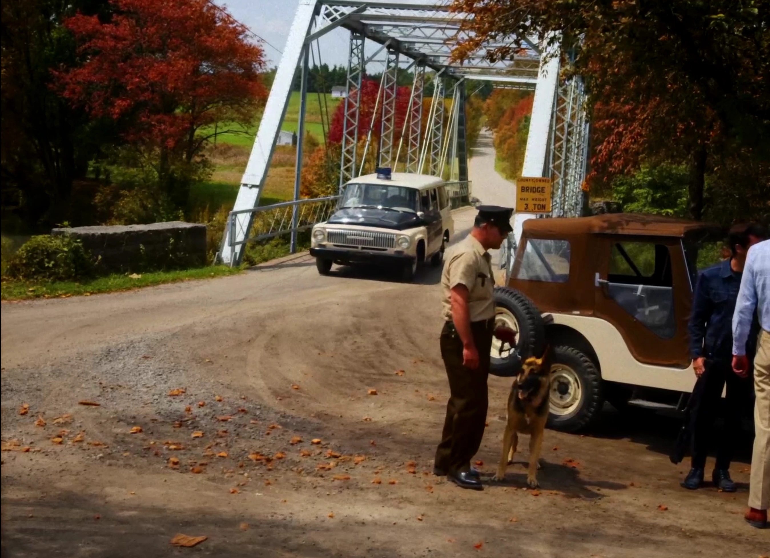 Colourised film still with period cars beside a steel bridge and autumn trees