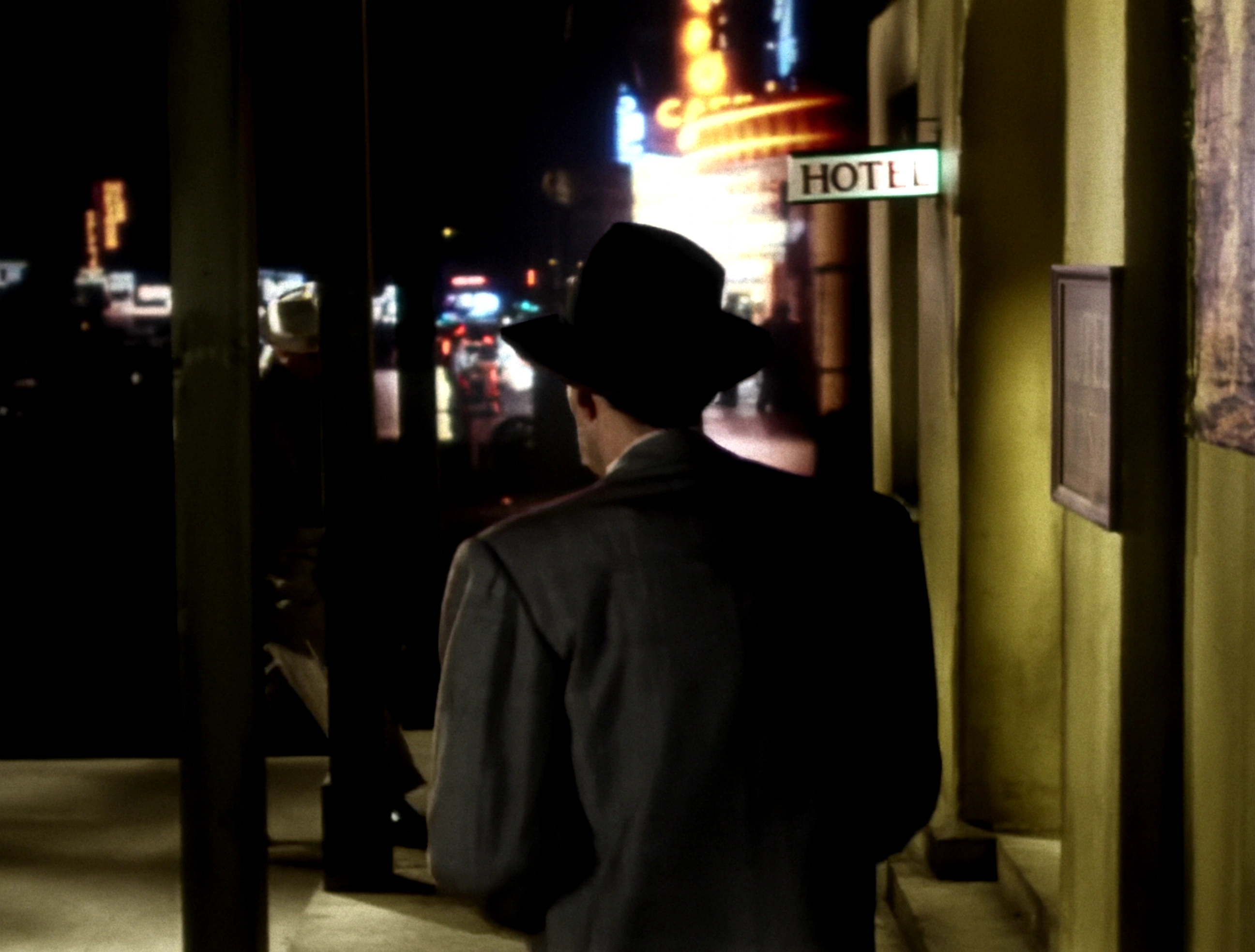 Film still of a figure walking past illuminated signs on a dark street